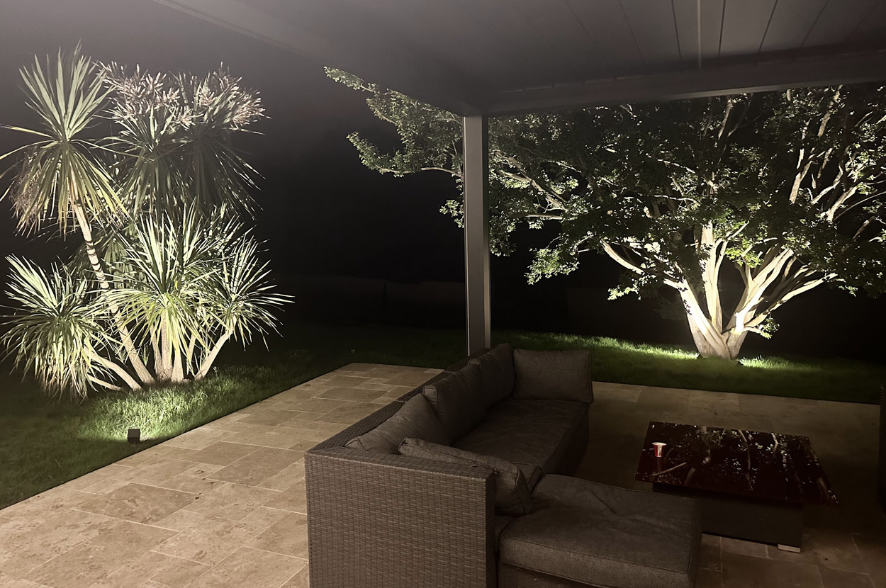 Éclairage extérieur de jardin mettant en valeur les arbres et les espaces verts autour d’une terrasse couverte dans le 64 (Pyrénées-Atlantiques).